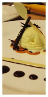 "vanilla ice cream on top of a touile paste cookie with a touile paste spoon, topped with chocolate cigarettes and garnished with chocolate, cream anglaise, and raspberry sauces"